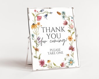 May include: A clear acrylic sign with a floral border featuring the text "THANK YOU for coming!" and "PLEASE TAKE ONE." The flowers are in shades of pink, yellow, blue, and purple. The sign is displayed on a silver stand.