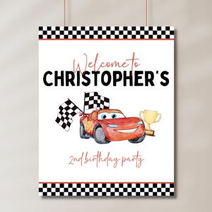 May include: A red race car with a checkered flag and a trophy, with the text "Welcome to Christopher's 2nd birthday party" on a white background with a black and white checkered border.