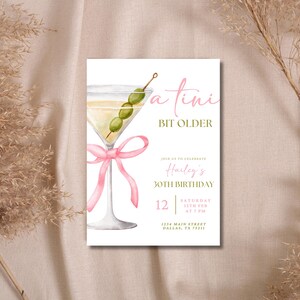 May include: A white invitation card with a pink ribbon and a martini glass with green olives. The text on the card reads "a tini bit older" and "Hailey's 30th Birthday".