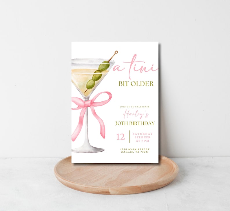 May include: A white invitation card with a pink ribbon and a martini glass with olives. The text on the card reads "a tini bit older" and "Harley's 30th Birthday". The invitation includes the date, time, and location of the party.