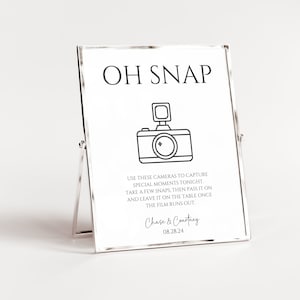 May include: A white sign with black text and a black and white illustration of a camera. The sign says "OH SNAP" and "USE THESE CAMERAS TO CAPTURE SPECIAL MOMENTS TONIGHT. TAKE A FEW SNAPS, THEN PASS IT ON AND LEAVE IT ON THE TABLE ONCE THE FILM RUNS OUT." The sign also includes the names "Chase & Courtney" and the date "08.28.24".