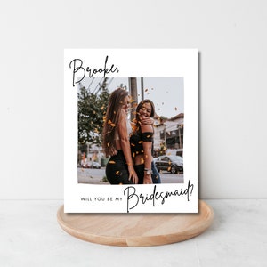 Może przedstawiać: Biała kartka z fotografią dw&oacute;ch kobiet, kt&oacute;re się uśmiechają. Tekst na kartce brzmi: "Brooke, Czy chcesz być moją druhną?"