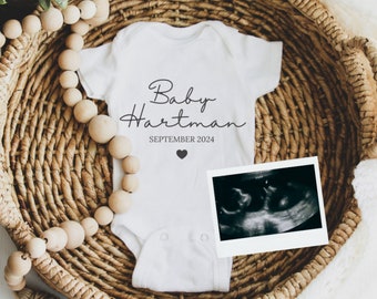 May include: White baby onesie with black text that reads "Baby Hartman SEPTEMBER 2024" and a small black heart. A black and white ultrasound image is next to the onesie.