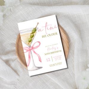 May include: A white invitation card with a pink ribbon and a martini glass with green olives. The text on the card reads "a tini bit older" and "Join us to celebrate Hailey's 30th Birthday".