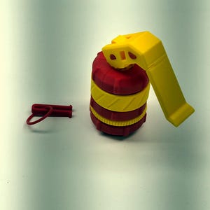 May include: A 3D-printed toy grenade in red and yellow. The grenade has a cylindrical body with yellow bands and a yellow handle. A small red pin is detached. The toy is designed to resemble a real grenade.