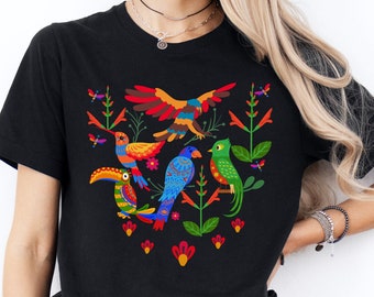 May include: Black t-shirt with a colorful design of birds and flowers. The birds are stylized and have bright colors, including red, blue, green, yellow, and orange. The flowers are red and pink.