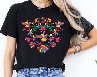 May include: Black t-shirt with a colorful embroidered design featuring birds and flowers. The design is reminiscent of traditional Mexican folk art.