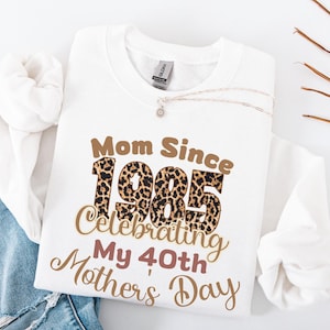 Puede incluir: Sudadera blanca con texto marrón que dice "Mom Since 1985 Celebrating My 40th Mother's Day". El número 1985 está impreso en un patrón de estampado de leopardo.