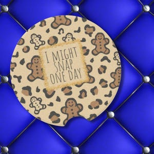May include: A round brown and black car coaster with a leopard print pattern and gingerbread men. The text "I might snap one day" is written in white on a brown rectangle.