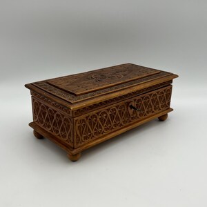 May include: A rectangular wooden box with intricate carved designs. The box is brown with a keyhole and small feet. The lid and sides feature detailed patterns, suggesting a decorative or storage purpose.