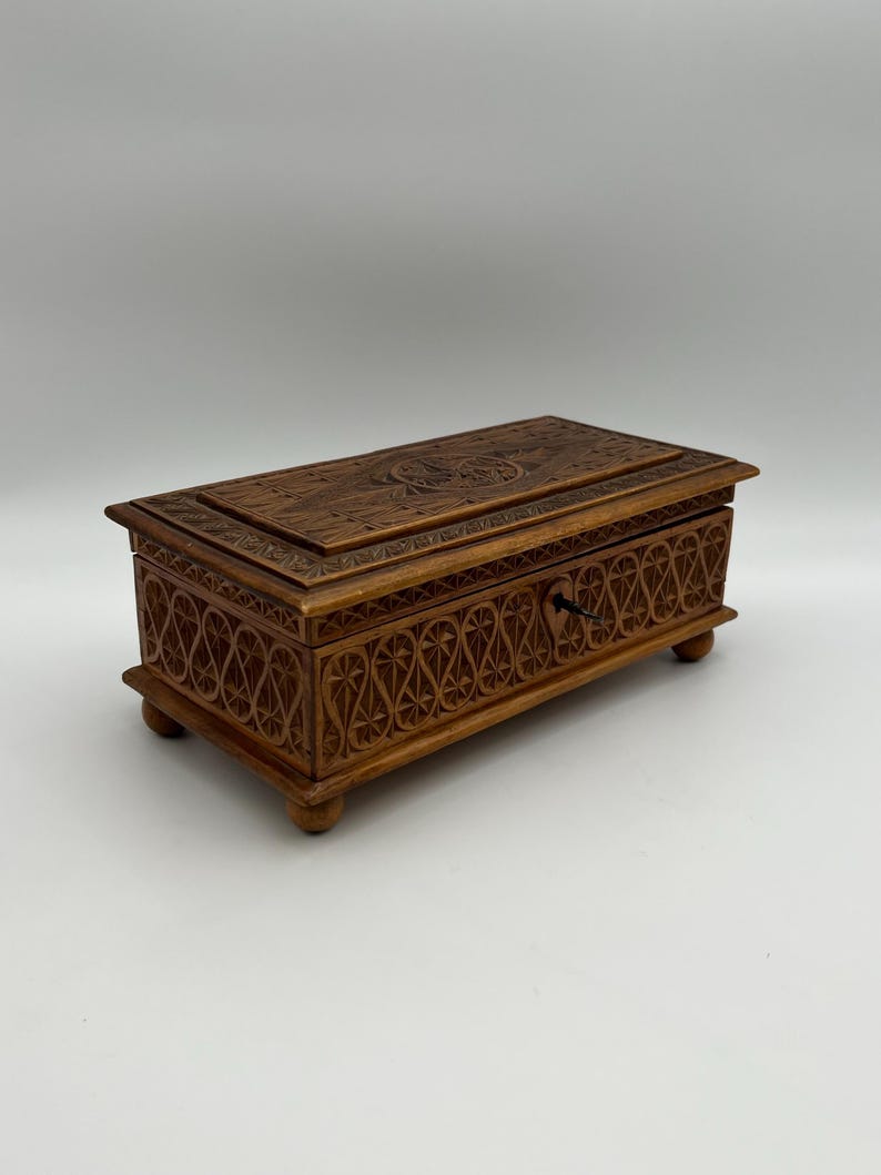 May include: A rectangular wooden box with intricate carved designs. The box is brown with a keyhole and small feet. The lid and sides feature detailed patterns, suggesting a decorative or storage purpose.