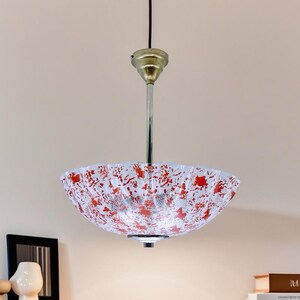May include: A white and red patterned glass pendant light fixture with a gold metal canopy and a silver chain.