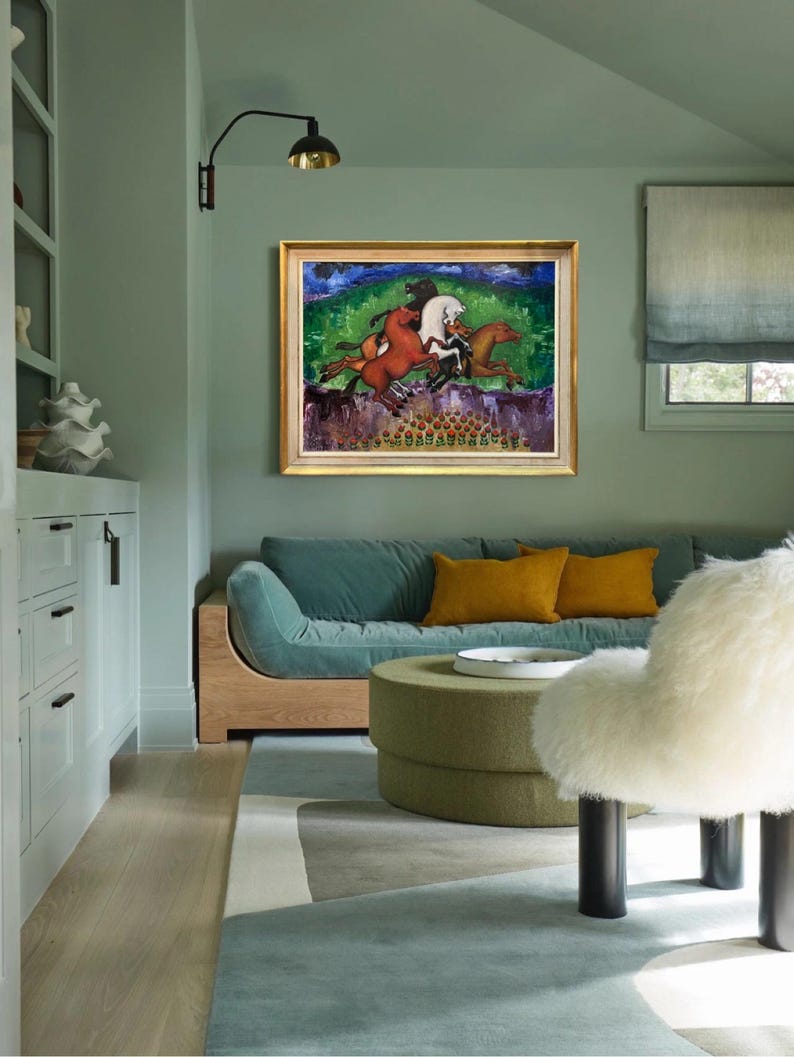 May include: An interior shot of a living room with a framed painting of horses. The painting has a gold frame and depicts horses in motion against a green and blue background. The room features a teal sofa, yellow pillows, and a green ottoman.
