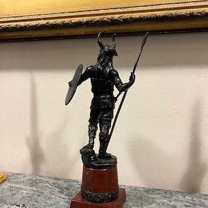 May include: A bronze sculpture of a Viking warrior holding a spear and shield, standing on a red marble base.