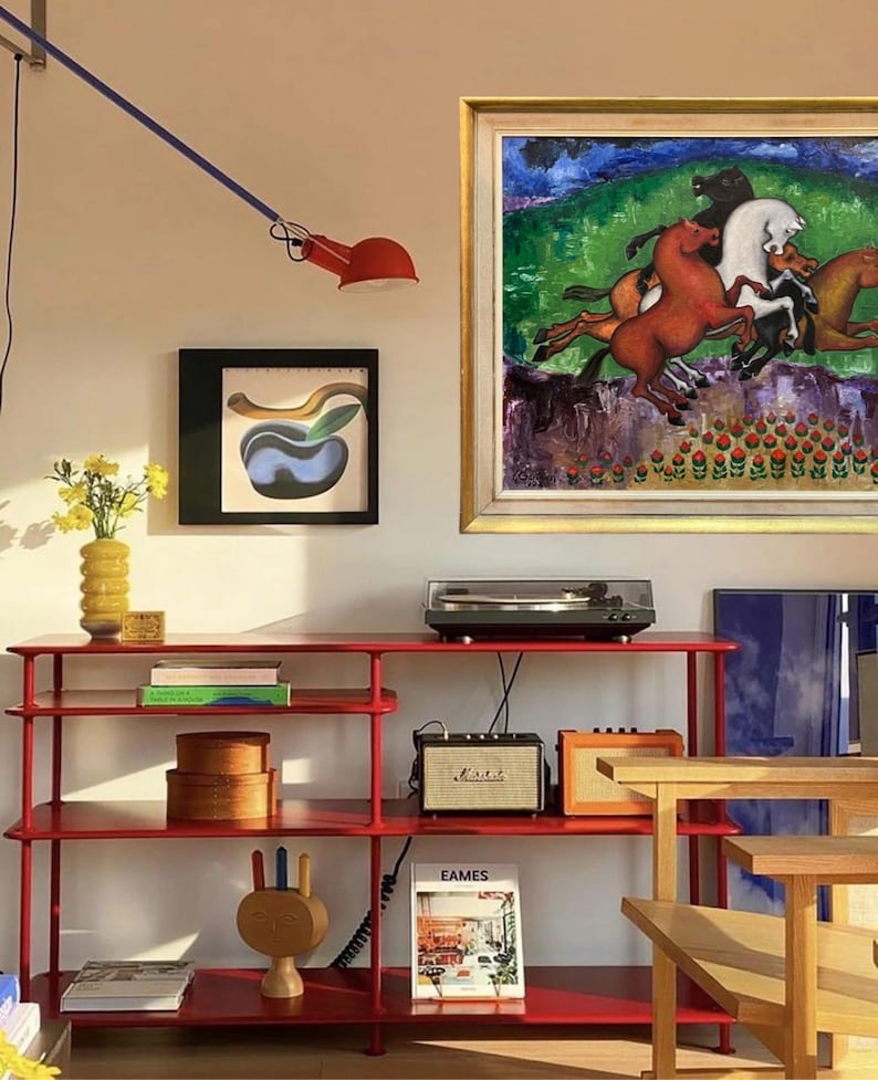 May include: A red metal shelving unit displays a turntable, speakers, and decorative items. A framed painting of horses hangs above the unit. A red lamp extends from the wall. A yellow vase holds flowers. A wooden sculpture and books are also visible.