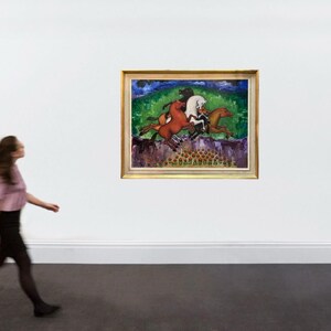 May include: A framed painting depicting several horses in motion, set against a backdrop of green foliage and a blue sky. The artwork features a gold frame and is displayed on a white wall. A person is walking in front of the painting.