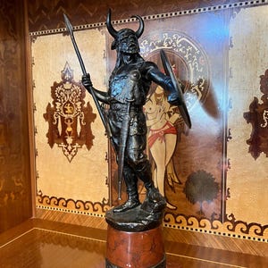 May include: A bronze sculpture of a warrior holding a spear and shield, standing on a red marble base.