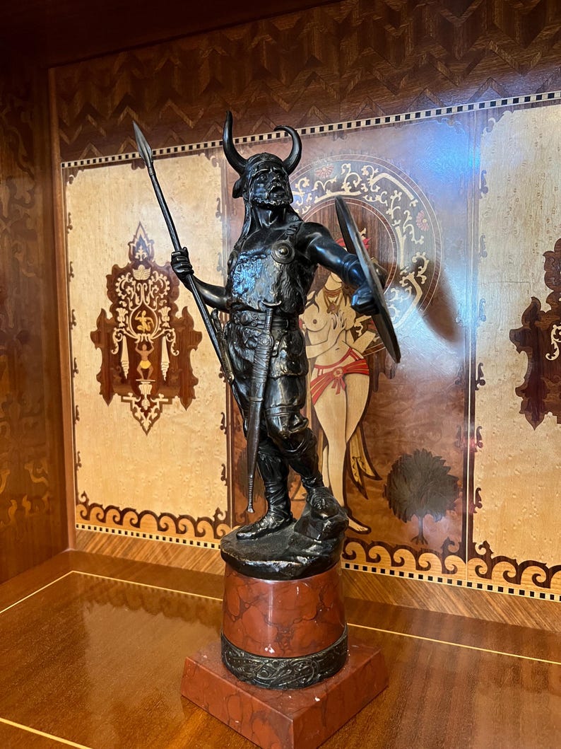 May include: A bronze sculpture of a warrior holding a spear and shield, standing on a red marble base.