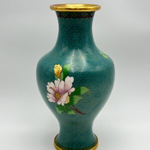 Puede incluir: Jarr&oacute;n de cloisonn&eacute; turquesa con borde y base dorados. El jarr&oacute;n presenta un dise&ntilde;o floral con p&eacute;talos rosas y blancos, hojas verdes y capullos amarillos. El cuerpo tiene un patr&oacute;n repetitivo en oro.