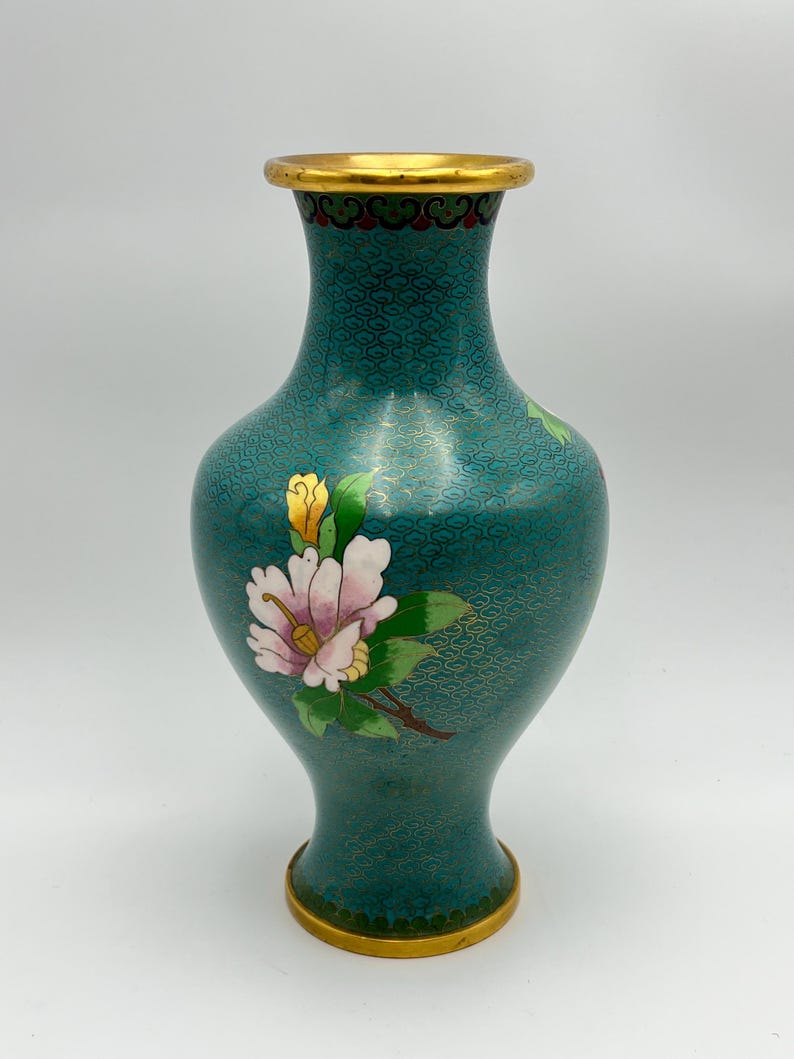 Puede incluir: Jarr&oacute;n de cloisonn&eacute; turquesa con borde y base dorados. El jarr&oacute;n presenta un dise&ntilde;o floral con p&eacute;talos rosas y blancos, hojas verdes y capullos amarillos. El cuerpo tiene un patr&oacute;n repetitivo en oro.