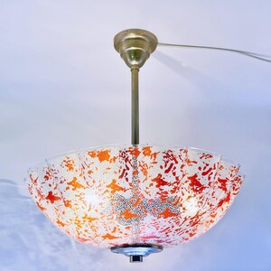 May include: A white and orange glass ceiling light fixture with a scalloped edge. The light fixture is hanging from a gold metal chain.