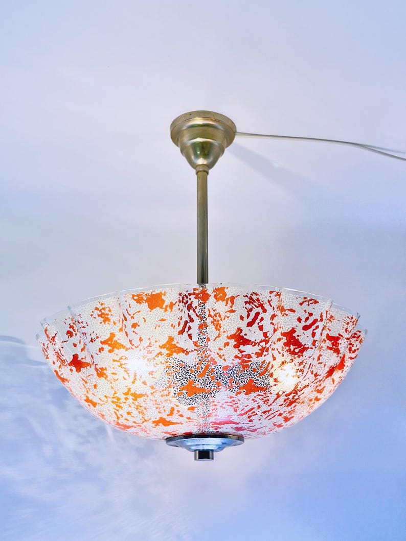 May include: A white and orange glass ceiling light fixture with a scalloped edge. The light fixture is hanging from a gold metal chain.