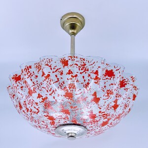 May include: A red and white patterned glass ceiling light fixture with a brass hanging rod.