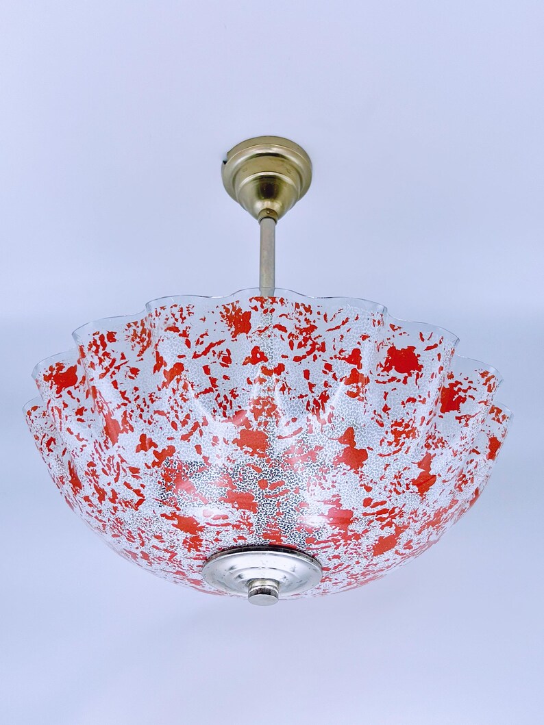 May include: A red and white patterned glass ceiling light fixture with a brass hanging rod.