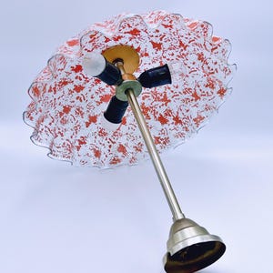 May include: A white and red glass lampshade with a ruffled edge and a silver metal base. The lampshade has a speckled pattern of red paint.