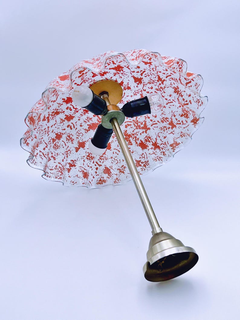 May include: A white and red glass lampshade with a ruffled edge and a silver metal base. The lampshade has a speckled pattern of red paint.