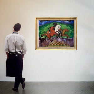 May include: A framed painting depicting three horses in motion, with riders, set against a green and blue landscape. The artwork is displayed in a gallery setting, with a person in the foreground.