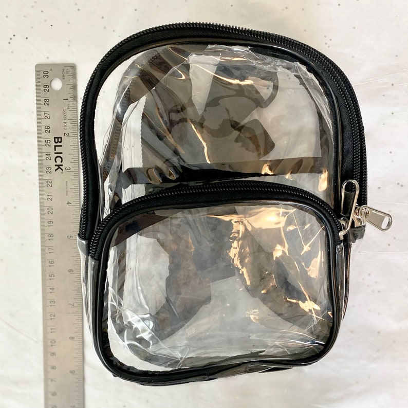 May include: Clear plastic backpack with black zipper and trim. The backpack has two compartments.