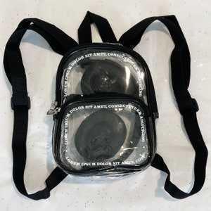 May include: A clear plastic backpack with black adjustable straps. The backpack has two clear compartments with black trim and white text that reads "LOREM IPSUM DOLOR SIT AMET, CONSECTETUER ADIPISCING".