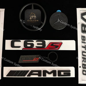 Pode incluir: Um conjunto de emblemas de carro pretos e vermelhos com o texto "V8 BITURBO", "C63 S" e "AMG".