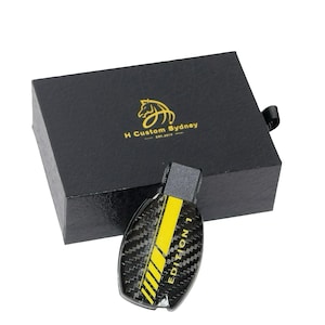 May include: A black box with a gold horse logo that says "H Custom Sydney Est. 2017" and a black and yellow carbon fiber key fob with the text "EDITION 1" in yellow.