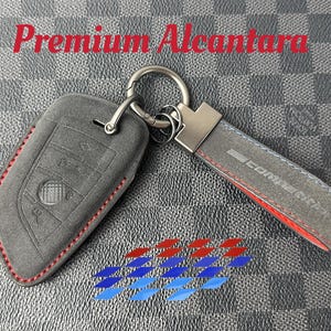 May include: A grey Alcantara key fob cover and matching keychain with red stitching. The keychain has a grey strap with "Competition" text and a red edge. The image also includes the text "Premium Alcantara".