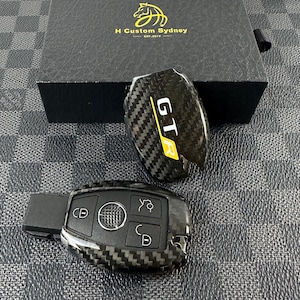 May include: A black carbon fiber key fob with a yellow "GT3" logo. The key fob is on a gray and white checkered background.