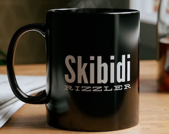以下が含まれることがあります： 「Skibidi Rizzler」の文字が薄いグレーでプリントされた黒いセラミックマグカップ。マグカップから湯気が立ち上り、温かい飲み物を連想させます。マグカップは木製の表面に置かれています。
