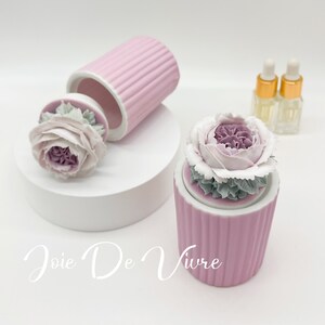 May include: A pink ceramic diffuser with a white and green floral design. The diffuser is labeled "Joie De Vivre".