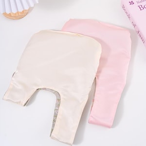May include: Two reusable shopping bags. One is a pale cream colour, and the other is a soft pink. Both bags are made of a silky material. The cream-coloured bag has a floral pattern visible on the inside. The bags are laying on a white surface.