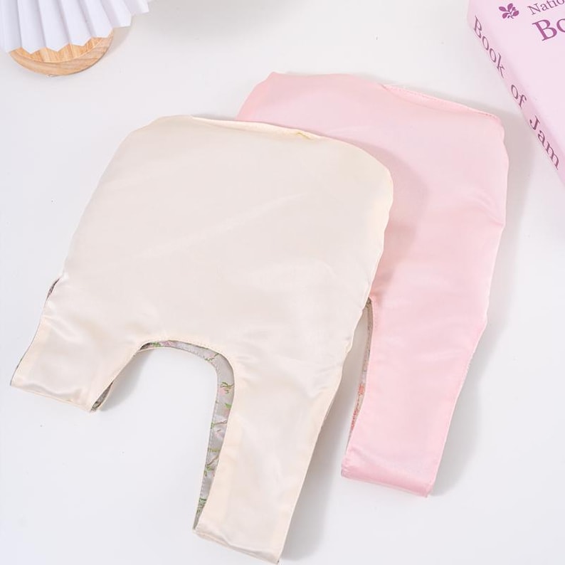 May include: Two reusable shopping bags. One is a pale cream colour, and the other is a soft pink. Both bags are made of a silky material. The cream-coloured bag has a floral pattern visible on the inside. The bags are laying on a white surface.