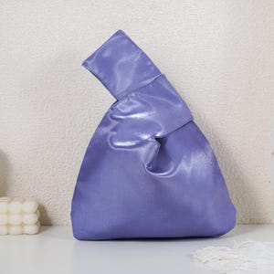 May include: A vibrant purple satin handbag featuring a unique Japanese-style knot handle design. The bag has a smooth, reflective finish and a triangular silhouette with one handle longer than the other, allowing it to loop through for closure.