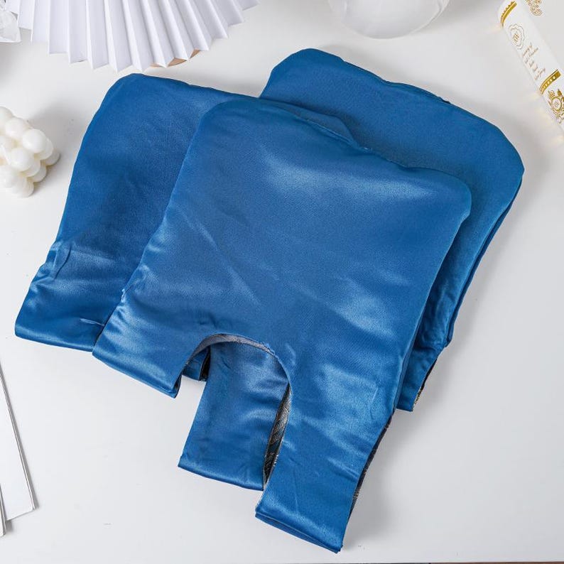 May include: Three blue satin shopping bags are displayed on a white surface. The bags have a glossy sheen and a classic tote bag design with a handle opening. The bags are empty and folded.