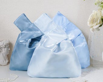 May include: Three satin knot bags in varying shades of blue, ranging from a light sky blue to a deeper medium blue. Each bag features a smooth, lustrous finish with a single integrated handle formed by the knotted fabric design at the top.