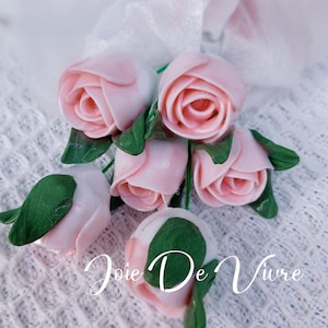 Könnte beinhalten: Ein Strauß aus sechs rosa Stoffrosen mit grünen Blättern. Die Rosen sind in einer Traube angeordnet und haben ein zartes, realistisches Aussehen. Der Text "Joie De Vivre" ist in der unteren rechten Ecke des Bildes sichtbar.