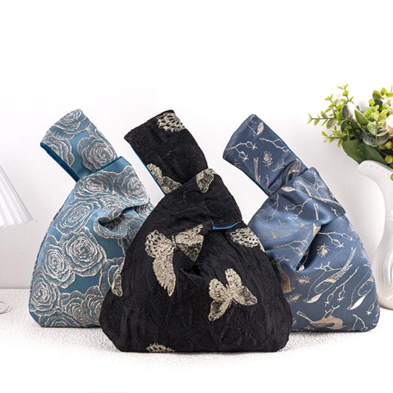 May include: Three decorative knot bags in blue and black. The blue bags feature floral and botanical patterns, while the black bag has a butterfly design. Each bag has a knotted handle and a contrasting blue interior.