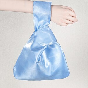 May include: A light blue satin knot bag featuring a triangular silhouette with a single handle loop. The fabric has a smooth, reflective finish and is constructed with a folded design where one handle passes through the other to create a secure closure.