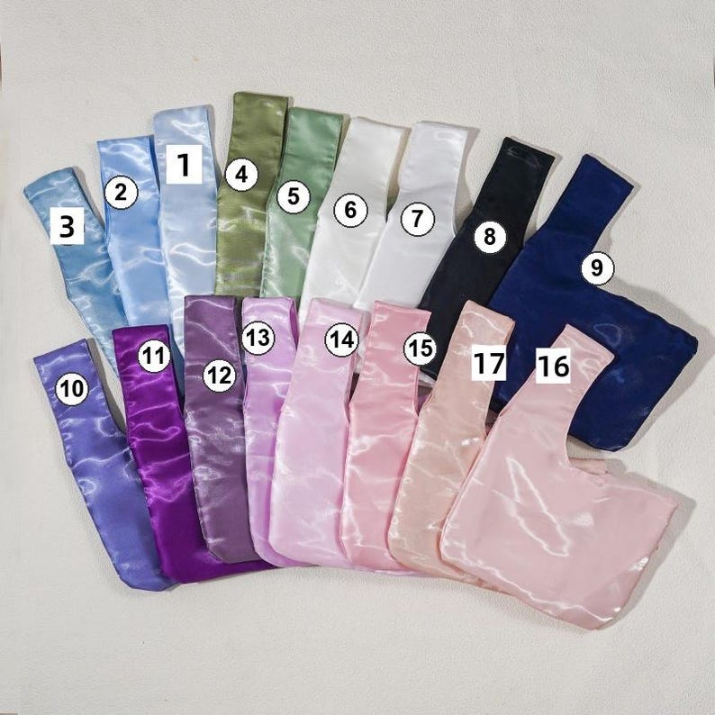 May include: A collection of seventeen satin fabric bags in various colors, each labeled with a numbered white circle. The colors include shades of blue, green, white, black, purple, and pink. Each bag features a single handle design.