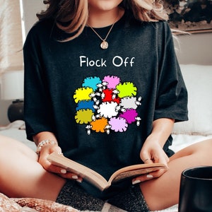May include: A black t-shirt with a graphic of colourful sheep and the text "Flock Off".
