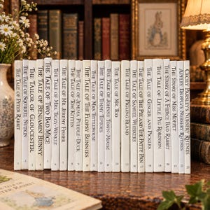 Op de afbeelding: Een verzameling van drieëntwintig witte boeken met harde kaft op een rij, elk met zwarte tekst op de rug met titels zoals The Tale of Peter Rabbit, The Tale of Squirrel Nutkin en Cecily Parsley's Nursery Rhymes.